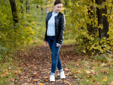 Autumn Park 'ta deri ceketli hoş bir kadın. Güzel Park sokağı. Sonbaharın parlak renkleri