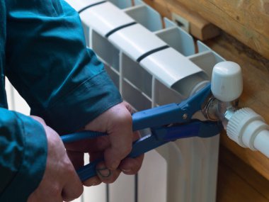 Adam somunu radyatöre sıkıyor. Isıtma pillerinin kurulumu. Tesisatçı işi..
