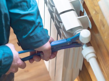 Adam somunu radyatöre sıkıyor. Isıtma pillerinin kurulumu. Tesisatçı işi..