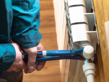 Adam somunu radyatöre sıkıyor. Isıtma pillerinin kurulumu. Tesisatçı işi..