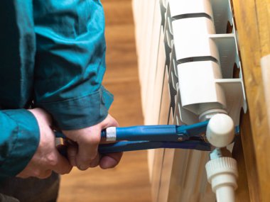 Adam somunu radyatöre sıkıyor. Isıtma pillerinin kurulumu. Tesisatçı işi..