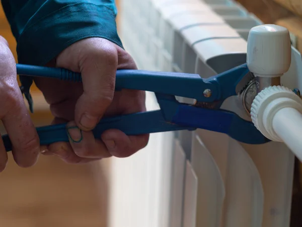 Adam somunu radyatöre sıkıyor. Isıtma pillerinin kurulumu. Tesisatçı işi..