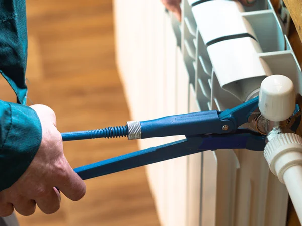 Adam somunu radyatöre sıkıyor. Isıtma pillerinin kurulumu. Tesisatçı işi..