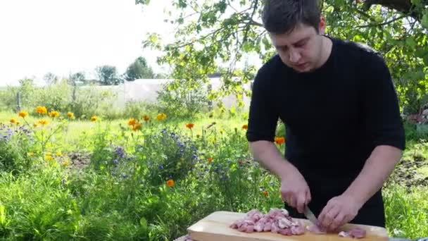 Un hombre corta carne en una tabla en un área suburbana. un joven con chaqueta negra prepara cerdo fresco — Vídeos de Stock