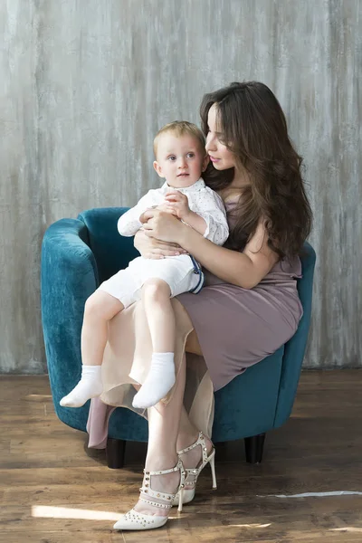 Oğlu ile hamile bir kız. Gri bir duvara bir sandalyede oturan.