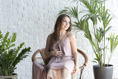 Hamile kız beyaz tuğla zemin üzerine bir sandalyede oturan.