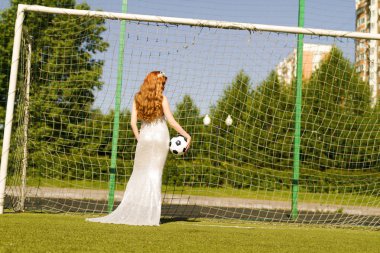 Kızıl saçlı bir kız futbol gol geri beyaz bir elbise bir top ile standları.