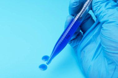 Eldivenli elini bir laboratuvar pipet mavi sıvı ile mavi bir arka plan üzerinde tutar..