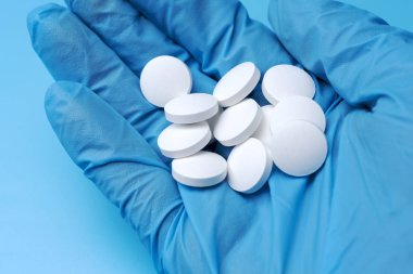 Mavi eldivenli yakın plan. Mavi arka planda beyaz haplar var. Laboratuvarda tıbbi ürün..