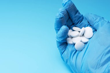 Mavi eldivenli yakın plan. Mavi arka planda beyaz haplar var. Laboratuvarda tıbbi ürün..