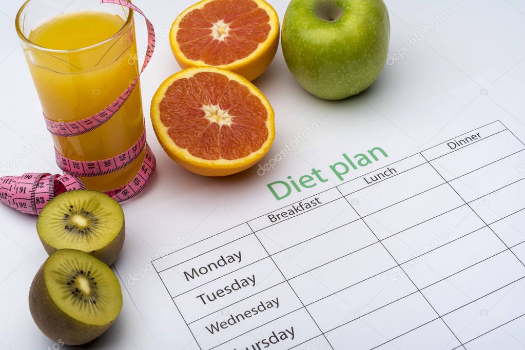 Diet plan on a piece of paper, next to a glass of orange juice. Fresh grapefruit, kiwi and Apple with centimeter on white background. The concept of healthy eating.
