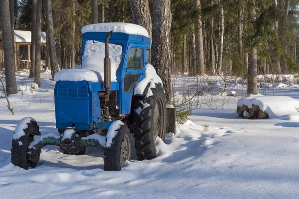 Snow-covered tractor in the woods near the village. Pine forest on a Sunny winter day.