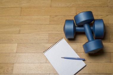 Sağlıklı bir beden sağlıklı bir zihin. Bir kağıt defter ve ahşap zemin üzerinde bir dumbbell. Sağlıklı bir yaşam tarzı, fitness kavramı.