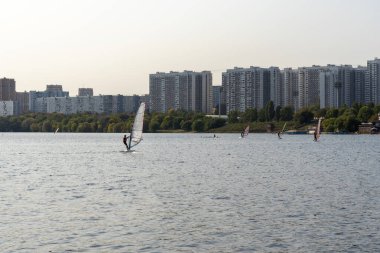 Rüzgâr sörfçüsü. Adam gökdelenlerin arka planında sörf yapıyor. Rüzgâr sörfü tahtasındaki adam. Şehirde rüzgar sörfü. Su sporları. Yelkenliyle sörf yapıyor..