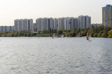 Rüzgâr sörfçüsü. Adam gökdelenlerin arka planında sörf yapıyor. Rüzgâr sörfü tahtasındaki adam. Şehirde rüzgar sörfü. Su sporları. Yelkenliyle sörf yapıyor..