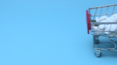 Mavi arka planda alışveriş arabasındaki haplar. İlaç ve bağımlılık kavramı.