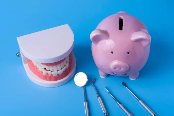 Piggy Bank on a blue background and dental instruments. The concept of saving money for the manufacture of dental implants and treatment.