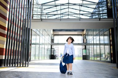 8 yaşındaki mutlu kız öğrenci okul bahçesinde sırt çantasıyla geziyor ve öğleden sonra kameraya yakından bakıyor.