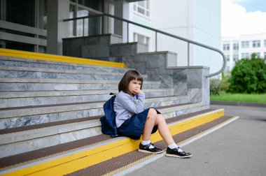 8 yaşındaki mutlu kız öğrenci okul bahçesinde sırt çantasıyla geziyor ve öğleden sonra kameraya yakından bakıyor.