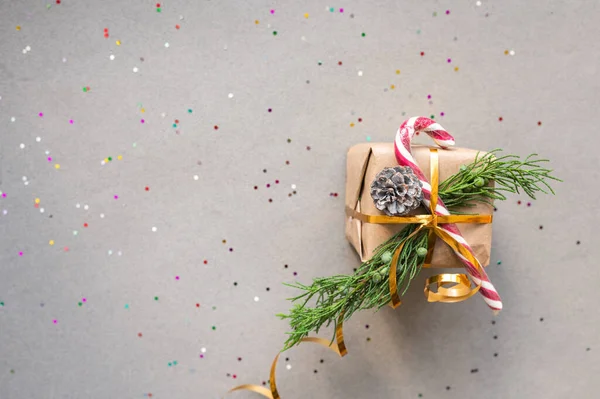 带有冷杉枝条的牛皮纸和灰色背景的棒棒糖中的圣诞礼物 配以彩色糖果 并附有文字圣诞概念 — 图库照片