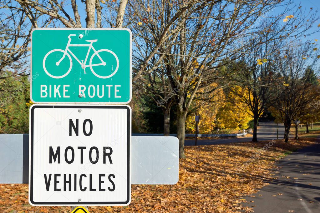 The season is autumn, thus this city sign gives awareness of a bike route and no motor vehicles allow.