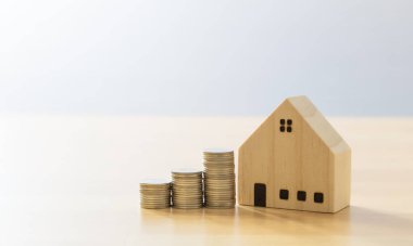 Ahşap ev modeli ve tahta panelde yığınla bozuk para. Bir konsept için para biriktirmek,