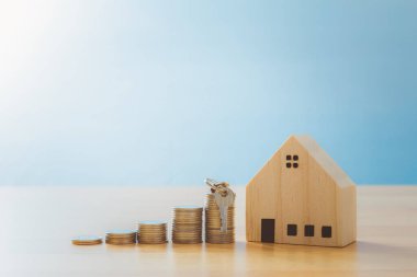 Model evi olan bozuk paraların önüne yerleştirilmiş anahtar. Mülk merdiveni, ipotek ve emlak yatırımları için anahtar ev konseptine sahip bir model ev. Emeklilik ya da ev almak için para biriktirme