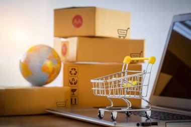 Müşterilere teslim etmek için paket kutusunun önüne dizilmiş bir dizüstü bilgisayarda alışveriş arabası ya da tramvay. Ticari işlemler internet üzerinden uzaktan satış için yürütüldü.