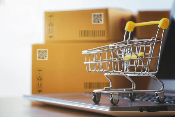 Müşterilere teslim etmek için paket kutusunun önüne dizilmiş bir dizüstü bilgisayarda alışveriş arabası ya da tramvay. Ticari işlemler internet üzerinden uzaktan satış için yürütüldü.