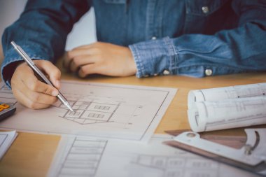 Elinde kalem tutan mimar ya da mühendis elinde ofis planıyla birlikte inşaat projesinin ekipmanlarını masaya koyuyor..