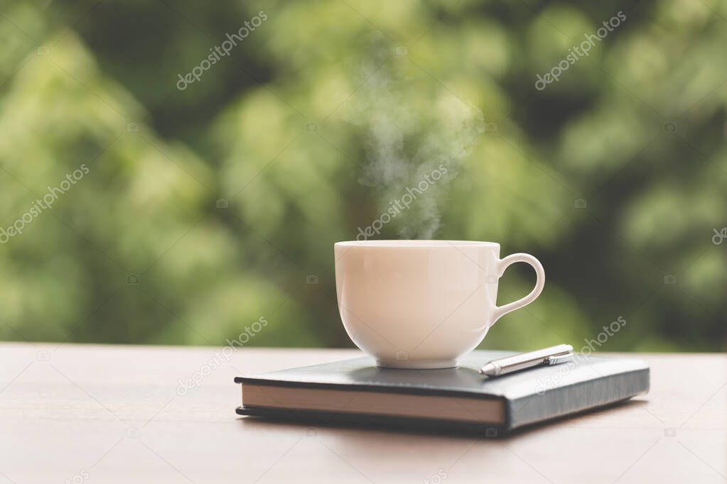 Hot coffee, smoke, with books and pens for note taking with beautiful nature background.