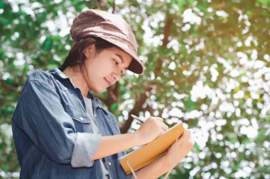 Asyalı kadın doğal arka plan üzerine notlar alıyor.