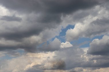 Mavi gökyüzünde beyaz ve gri bulutlar, bulutların arka planında gri bir duman bulutu