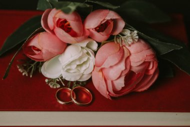 Kırmızı defterdeki alyanslar ve yapay şakayık buketi.