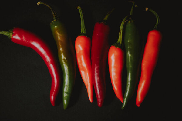 bunch of red orange and green chilli peppers on black background