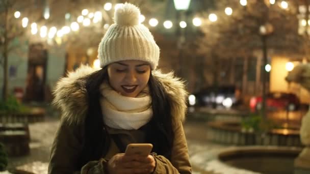 Beautiful Smiling Girl Messaging Smartphone Winter Street Christmas Lights Slow — Stockvideo