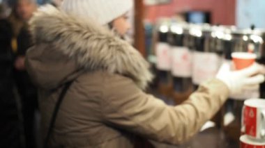 Young happy woman is buying hot punch in cold winter evening on street market in SLOW MOTION HD VIDEO. She is smiling and tasting her drink. Half speed.