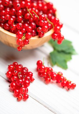 Beyaz ahşap masadaki bir kasede yaprakları olan taze kırmızı frenk üzümü. Sağlıklı organik yiyecekler, yaz vitaminleri, BIO virüsleri, doğal arka plan. Reklam metniniz için alanı kopyalayın.