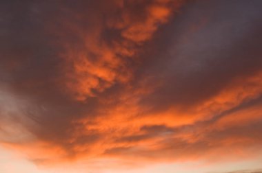 Gökyüzü arka planını ateşle. Gün batımında hafif bulutlar ve güneş ışığı. Birçok turuncu ton ve bulut deseni.