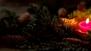 Karanlık arka planda mumlar ve 4K VIDEO 'da iğneler bulunan bir Noel süslemesi. Yakın çekim ve sığ alan derinliği. Noel tatili ve Yeni Yıl teması.