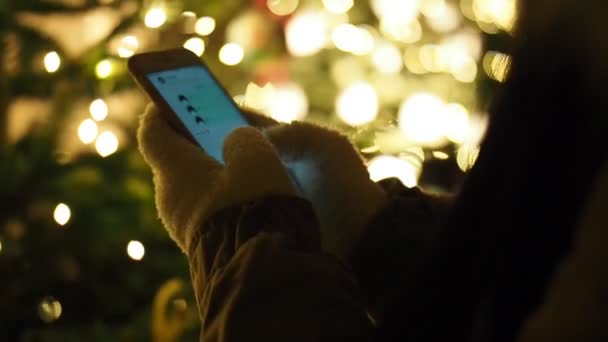 Vrouw Handen Handschoenen Sms Met Mobiele Telefoon Door Verlichte Kerstboom — Stockvideo