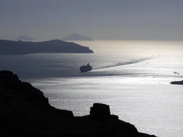 The silhouette of a luxury cruise ship in a bay near Fira. View of the mediterranean sea, islands and caldera during sunset.