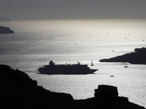 The silhouette of a luxury cruise ship in a bay near Fira. View of the mediterranean sea, islands and caldera during sunset.