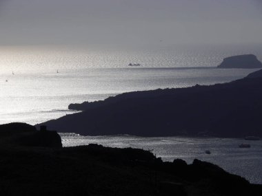 Fira yakınlarındaki bir körfezde lüks bir yolcu gemisinin silüeti. Gün batımında Akdeniz, adalar ve kalderanın manzarası.