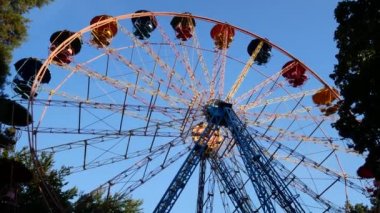 Dönme dolap, kamaraların yavaş hareketi, batan güneşin ışınlarında mavi gökyüzüne karşı. İnsansız eski dönme dolaplar..