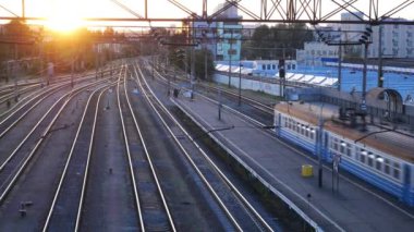 Bir yolcu treninin, batan güneşin arka planına karşı istasyondan geçişi. Güneşin raylardaki yansımaları uzaklığa doğru kayıyor.. 