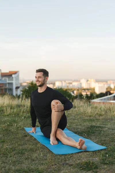 Image of young man stretching his body at sports ground outdoors