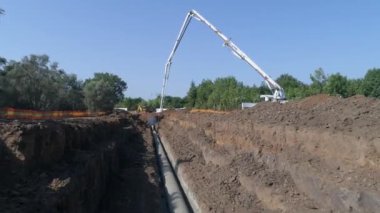 İnşaat alanının üzerinde bir hava aracı vuruldu. Boru hattı altyapısına çimento döken büyük beyaz bir vinç. İnşaatçılar dışarıda çalışıyor.