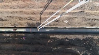 Boru hattının altyapısına beton döken büyük beyaz vinç üzerinde tepeden aşağı uçan drone görüntüsü. İnşaat alanında çalışan erkekler olarak.