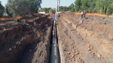 İnşaatçılar iş başında. Boru hattı altyapısına çimento döken büyük beyaz bir vinç. İnsansız hava aracı görüntüleri.